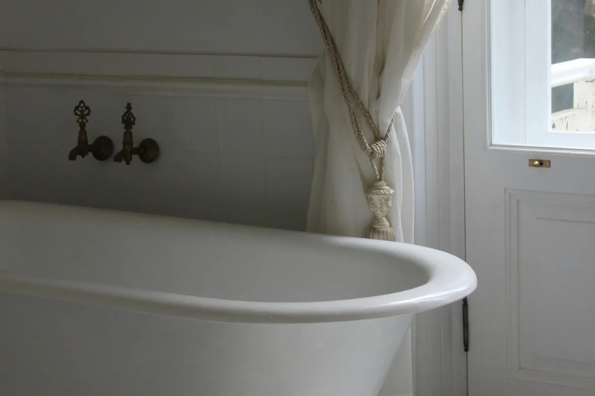 Bồn tắm chân sứ trắng cạnh cửa sổ, rèm voan buộc gọn