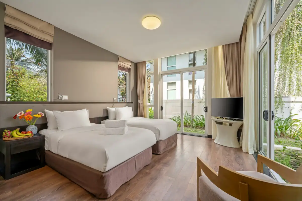 Phòng gia đình ở Huế: phòng hai giường đơn trải ga trắng, sàn gỗ, cửa kính lớn nhìn ra vườn